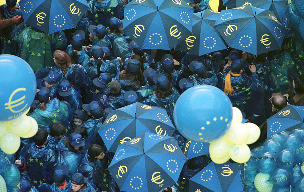 Euro balloons are prepared to be raised over a crowd of people dressed in European colours hoding Euro umbrellas at the European Council building Justus Lipsius as the European single currency is being launched in Brussels 31 December. (Photo by OLIVIER MATTHYS / BELGA / AFP) (Photo by OLIVIER MATTHYS/BELGA/AFP via Getty Images)