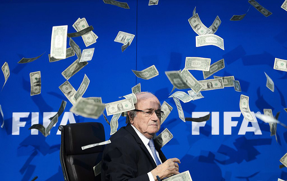 FIFA president Sepp Blatter looks on as fake dollar notes fly around him, thrown by a British comedian during a press conference at the FIFA world-body headquarter's on July 20, 2015 in Zurich. The 79-year-old Swiss official looked shaken as the notes thrown by Simon Brodkin, stagename Lee Nelson, fluttered around him in a conference hall at the FIFA headquarters. Brodkin was taken away in a Swiss police car after the stunt. AFP PHOTO / FABRICE COFFRINI / AFP / FABRICE COFFRINI (Photo credit should read FABRICE COFFRINI/AFP via Getty Images)